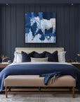 Modern bedroom with dark blue walls, a bed with white bedding and blue throw, and abstract art above the bed.