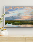 Framed landscape painting of a sunset over water on a wall above a wooden console table with decorative items.