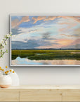 Framed landscape painting of a sunset over water on a wall above a wooden console table with decorative items.