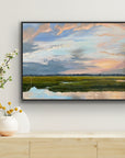 Framed artwork of a landscape with a river and sky, displayed on a wall above a wooden cabinet.