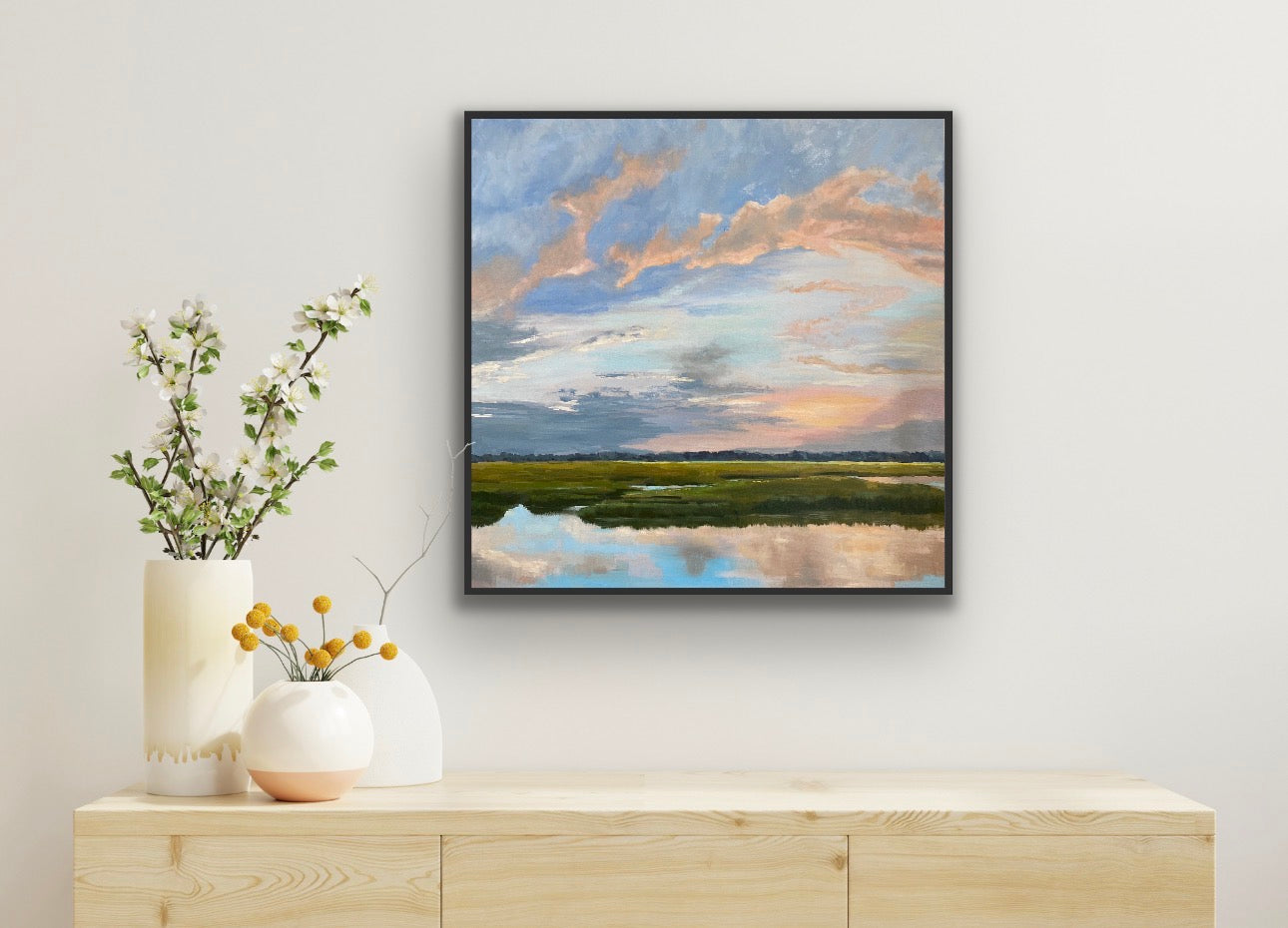 Framed artwork of a landscape with a river and sky above a wooden console table with decorative vases.